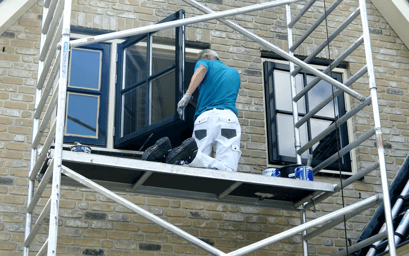Schilder van VON Garant werkt vanaf de steiger aan kozijnen